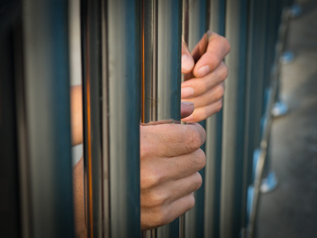 Hand of prisoner holding prison bars in jail.