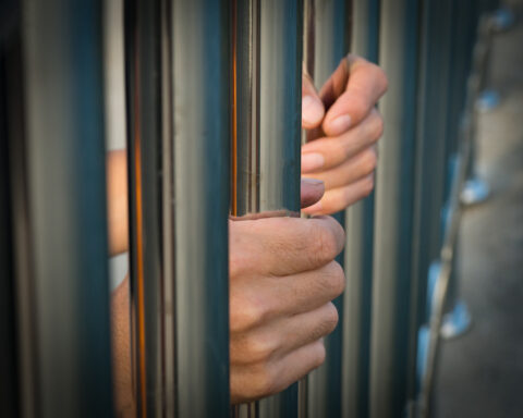 Hand of prisoner holding prison bars in jail.
