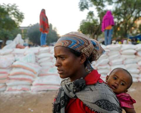 Woman carries an infant as she queues in line for food, at the Tsehaye primary school, in Shire